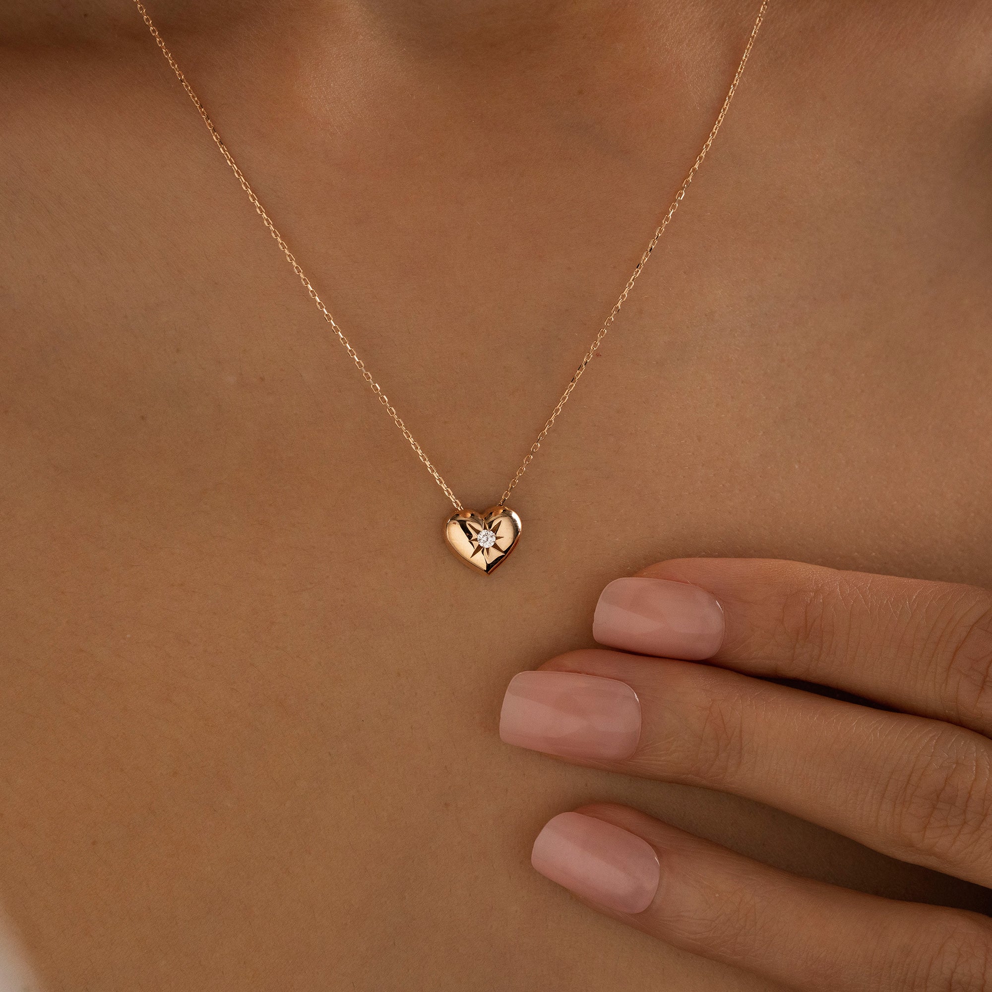 Arel Custom Jewelry 14k solid gold necklace featuring a polished puffed heart pendant with a starburst set center diamond on a model.
