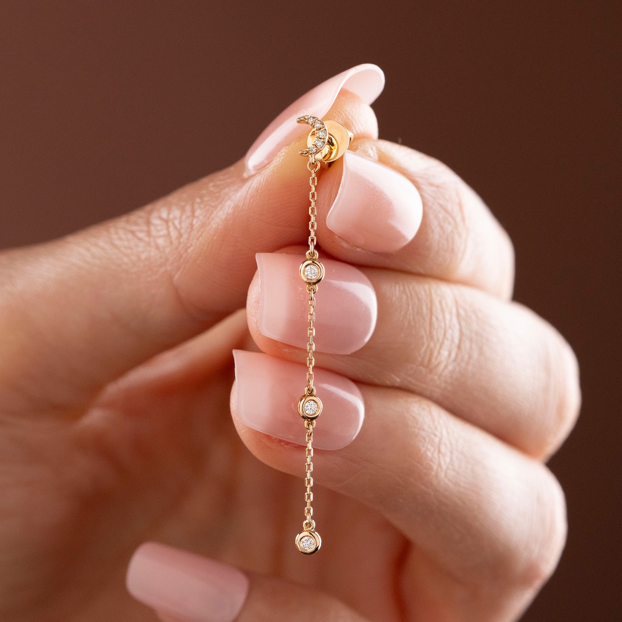 Arel Custom Jewelry 14k solid gold celestial crescent moon drop earring with dangling bezel set diamonds on a model.